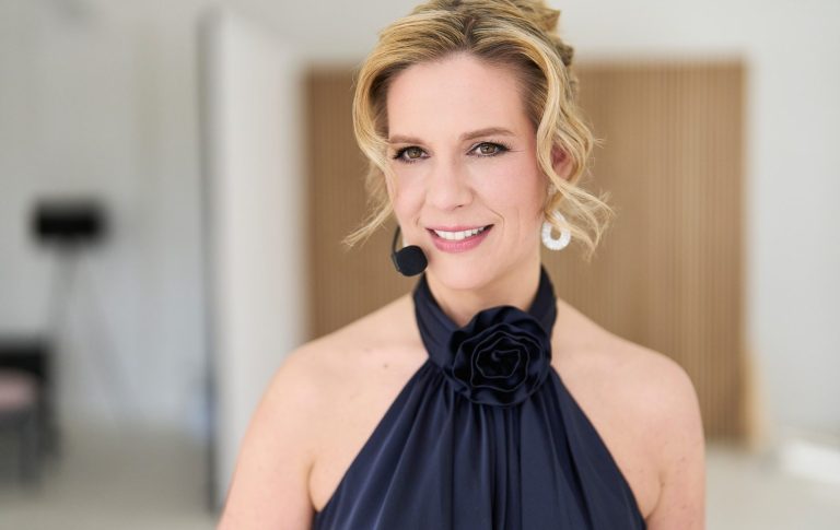 Natascha Enders trägt ein elegantes, schwarzes Oberteil und ein Mikrofon.