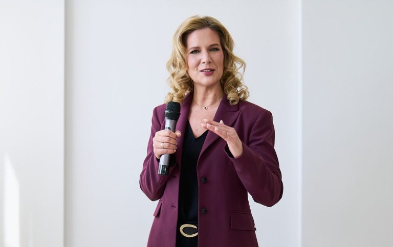 Natascha Enders in lila Blazer, spricht mit einem Mikrofon in der Hand.