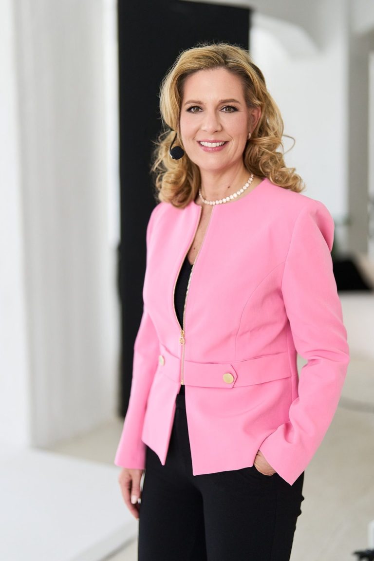 Natascha Enders in pinker Jacke, lächelt vor neutralem Hintergrund.